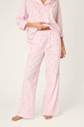 A person is standing barefoot on a neutral background, wearing P.J. Salvage Afterparty Poplin Stripe & Martini Print Pajama Pants with a coordinating light pink, long-sleeve top featuring a small print pattern, and lifting the top slightly to reveal the waistband.