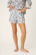 A person stands barefoot, adjusting the waistband of their Afterparty Poplin Stripe & Poodle Print Pajama Shorts by P.J. Salvage; they are also wearing a matching blue and white striped shirt with a portion of the upper body out of frame.