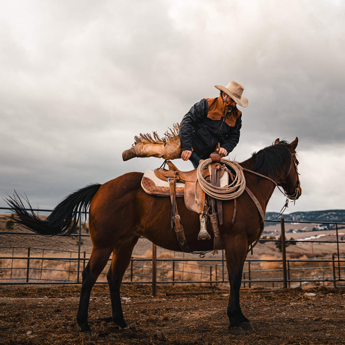 A cowboy in a black and coyote AUGUSTA jacket riding a horse, preparing to rope in an outdoor setting.