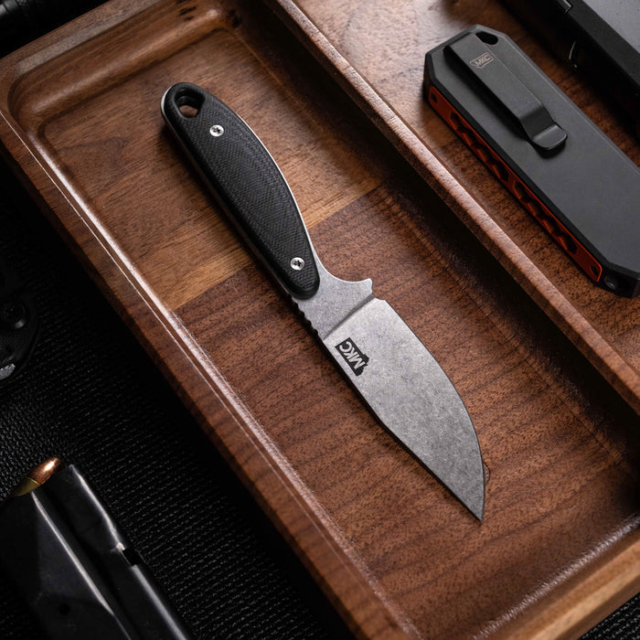 Black BADROCK knife with a textured handle displayed on a wooden tray alongside a tactical tool and other gear.