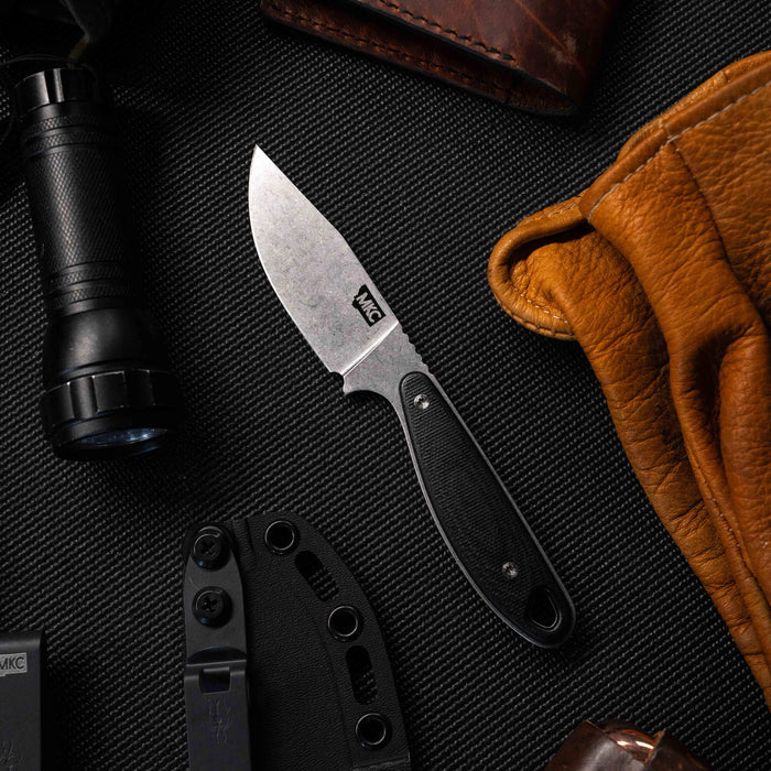 BADROCK knife in black with a textured handle, surrounded by a flashlight, leather gloves, and other tools.