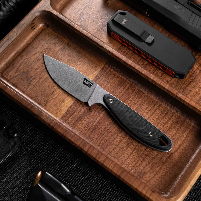 Montana Knife Company's BADROCK knife in black, displayed on a wooden tray with tactical gear and tools.