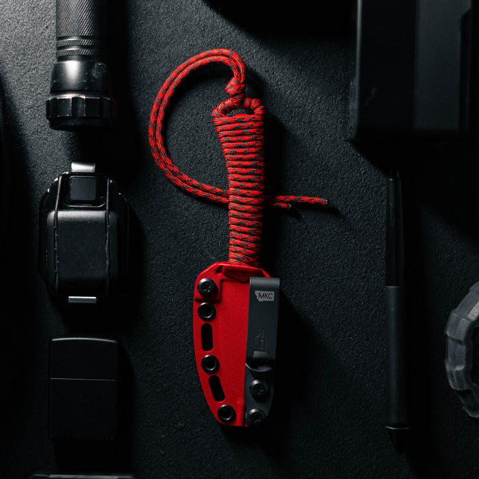 Black and red Blood Brothers Mini-Speedgoat 2.0 knife with a textured handle, surrounded by tactical gear and tools.