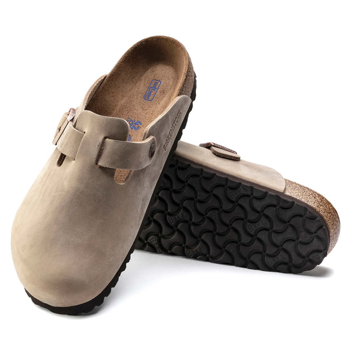 Pair of Birkenstock Boston clogs, one standing on heel to show black tread outsole, highlighting the footbed and sole design.