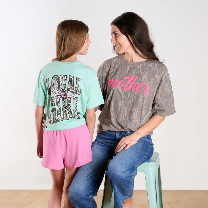 Two women wearing t-shirts with text and graphics, sitting on a stool.