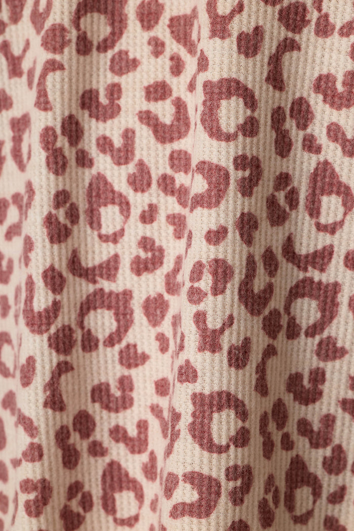 Close-up of a waffle-textured fabric with an allover leopard print pattern in dusty wine on a warm beige background.