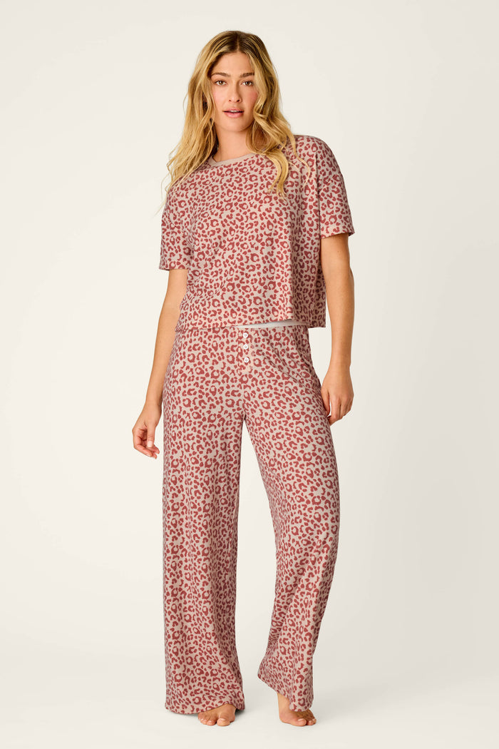 A woman stands barefoot against a plain light background wearing the P.J. Salvage Boyfriend Boxer Leopard Print Short Sleeve & Pants PJ Set, featuring a matching red leopard print with a short-sleeve top and wide-leg pants.