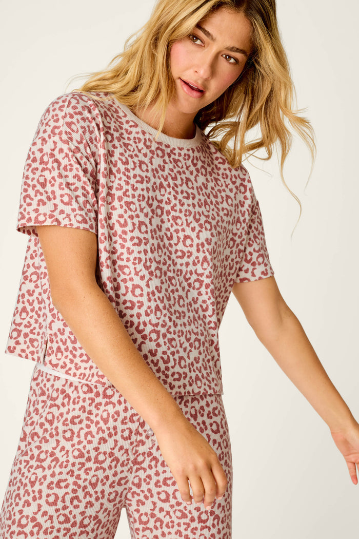 A woman with long blonde hair wears the P.J. Salvage Boyfriend Boxer Leopard Print Short Sleeve & Pants PJ Set, featuring a matching pink and white leopard print design, as she stands against a light background.