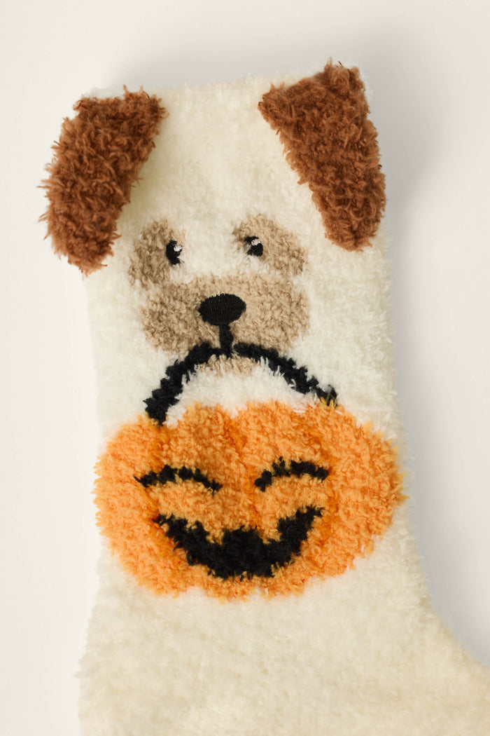 The P.J. Salvage Boyfriend Boxer Trick-or-Treating Dog Socks feature a fuzzy white design with a brown-eared dog face holding an orange jack-o-lantern in its mouth.
