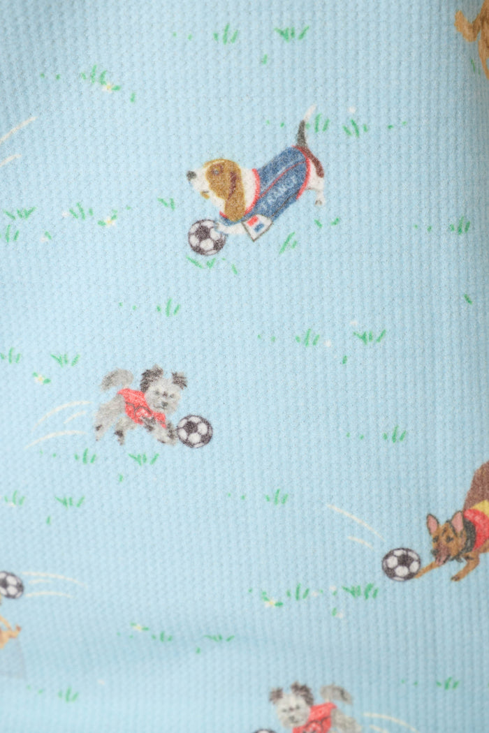 Blue fabric with a playful pattern of pups in outfits, soccer balls, and grassy fields.