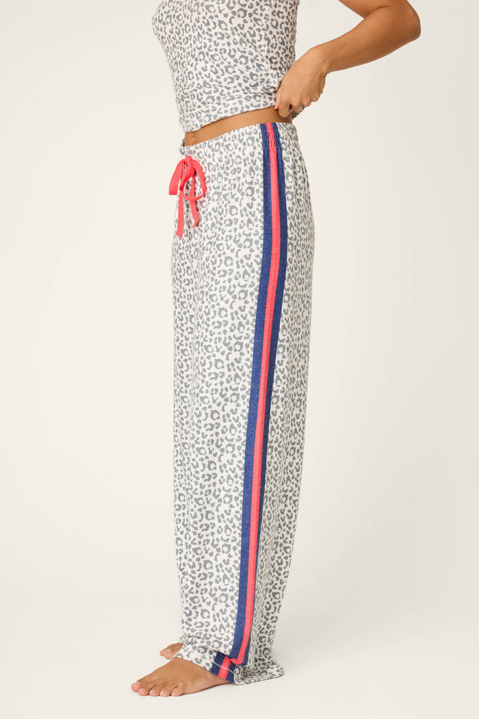 A person in P.J. Salvage Cat’s Meow Big Stretch Pajama Pants—peachy-soft leopard print jersey with red and blue side stripes and a red drawstring—stands barefoot on a light background, perfect for cozy nights in.