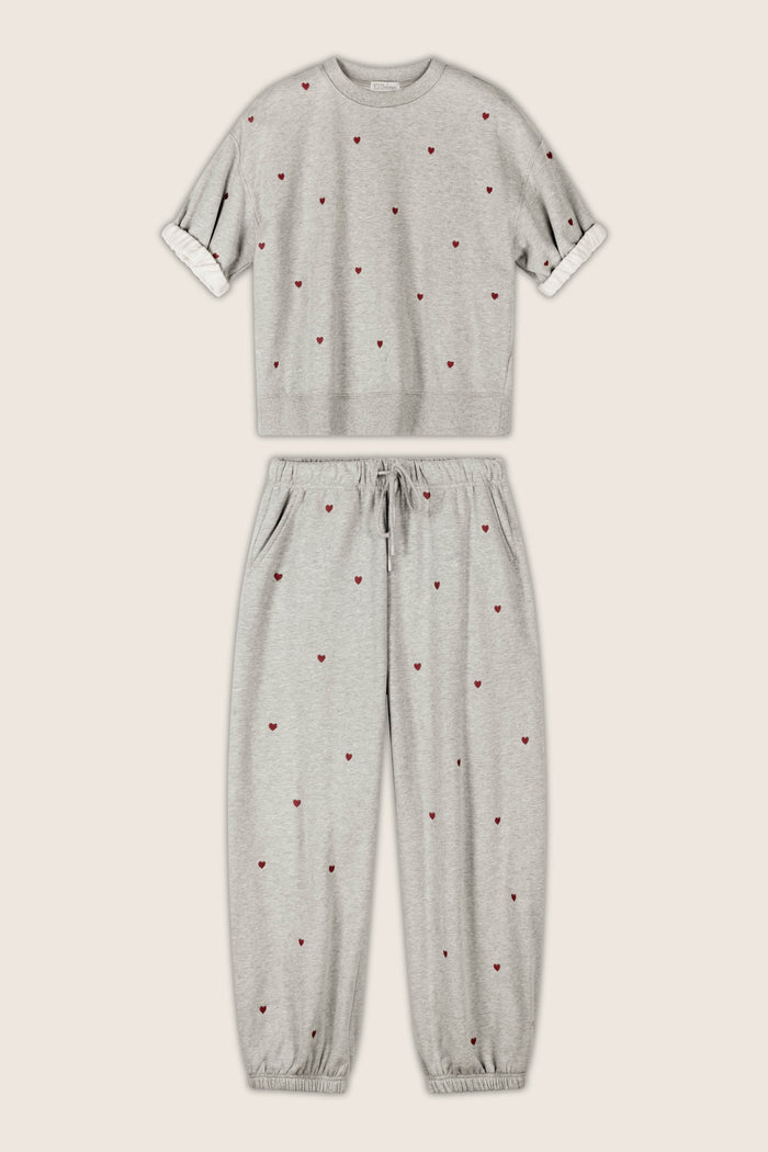 The P.J. Salvage C'est La Vie Embroidered Hearts Roll Back Short Sleeve Sweatshirt and coordinating jogger pants set, featuring small red heart embroidery, is displayed flat against a beige background. The jogger pants include a drawstring waist and elastic cuffs.