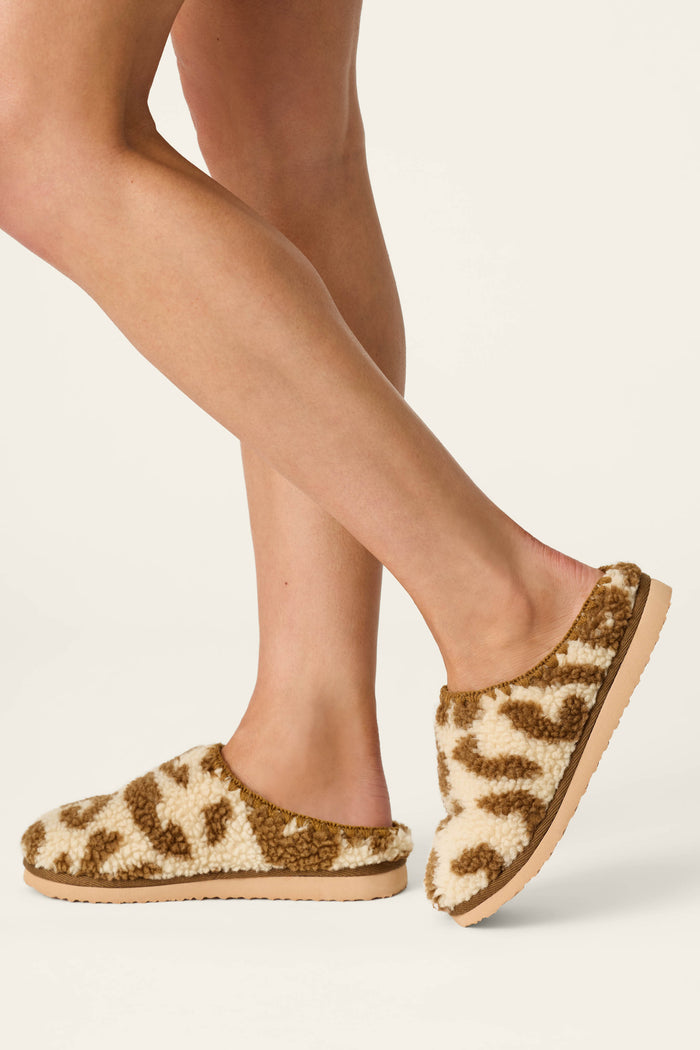 A person wearing P.J. Salvage Cheetah Bonita Dreams Cheetah Print Fuzzy Slippers stands on a light background.