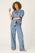 A person with curly hair wears the P.J. Salvage Classic Paisley Bandana Print 3-Piece Long Sleeve Flannel PJ Set, featuring a loose-fitting, blue paisley pattern. Standing barefoot against a light background, they have one arm raised while the other rests relaxed by their side.