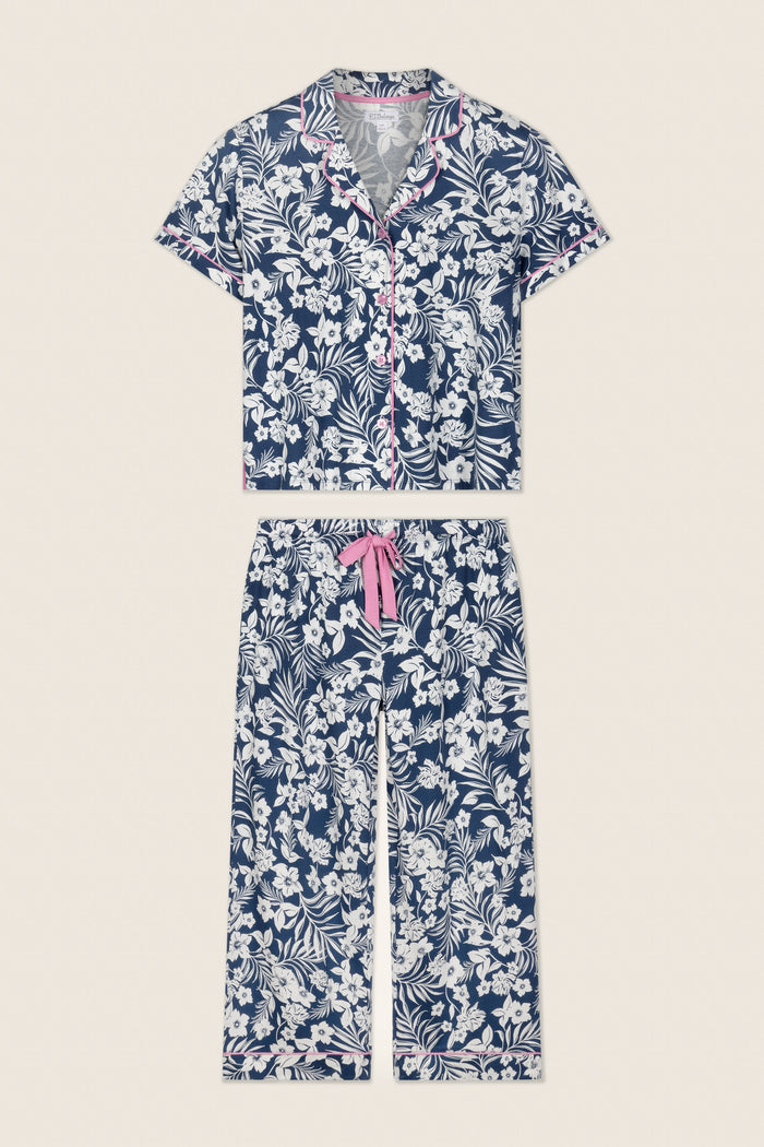 The P.J. Salvage Cotton Jersey Midnight Garden Cropped PJ Set features a navy and white floral short-sleeve button-up top, cropped pants with pink trim on the collar and cuffs, and a pink drawstring waist.