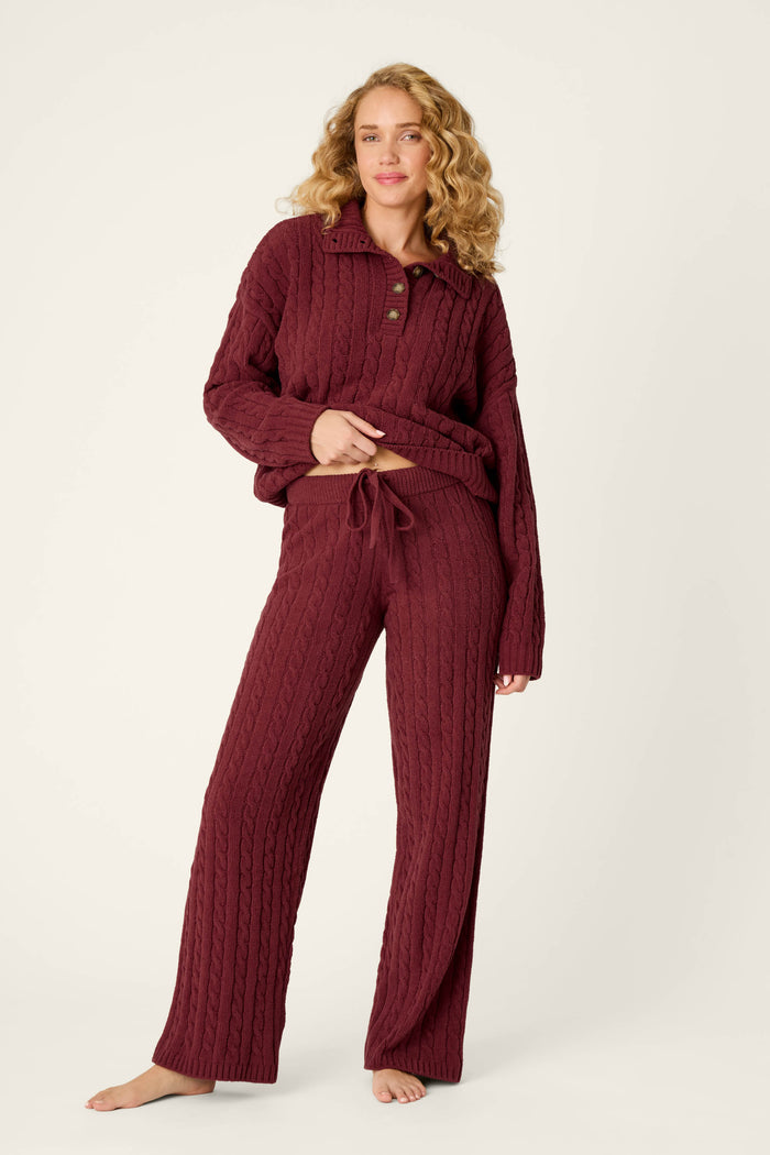 A woman models the P.J. Salvage Cozy Chenille Cable Knit Dark Wine Lounge Pants, barefoot against a plain light background, lifting her sweater slightly to reveal the drawstring waist.