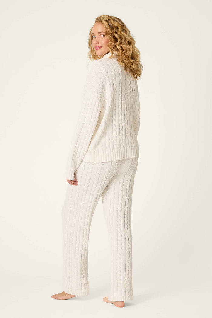 A woman with curly blonde hair models the P.J. Salvage Cozy Chenille Cable Knit Ivory Pullover Lounge Set, standing barefoot and turned slightly to the side against a plain light background.