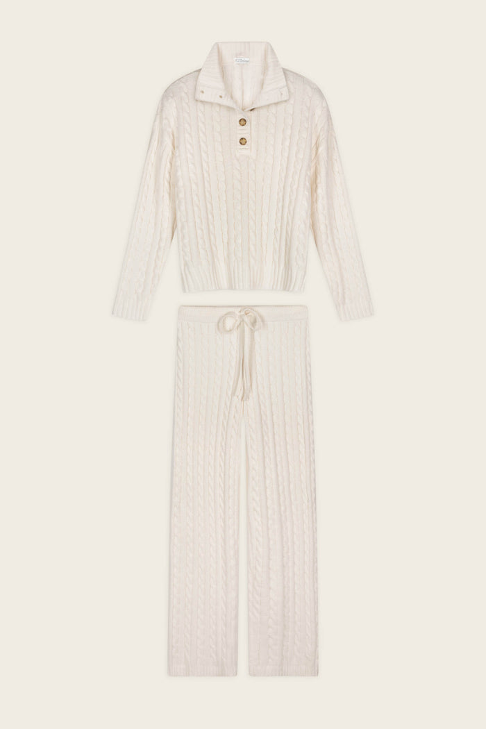 The P.J. Salvage Cozy Chenille Cable Knit Ivory Pullover Lounge Set features a long-sleeve, button-collar sweater and matching drawstring pants, both showcasing a cable knit pattern in a cream hue, displayed against a plain light background.