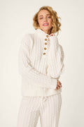 A person wearing the P.J. Salvage Cozy Chenille Cable Knit Ivory Pullover, featuring button details on the collar, stands against a plain light background.