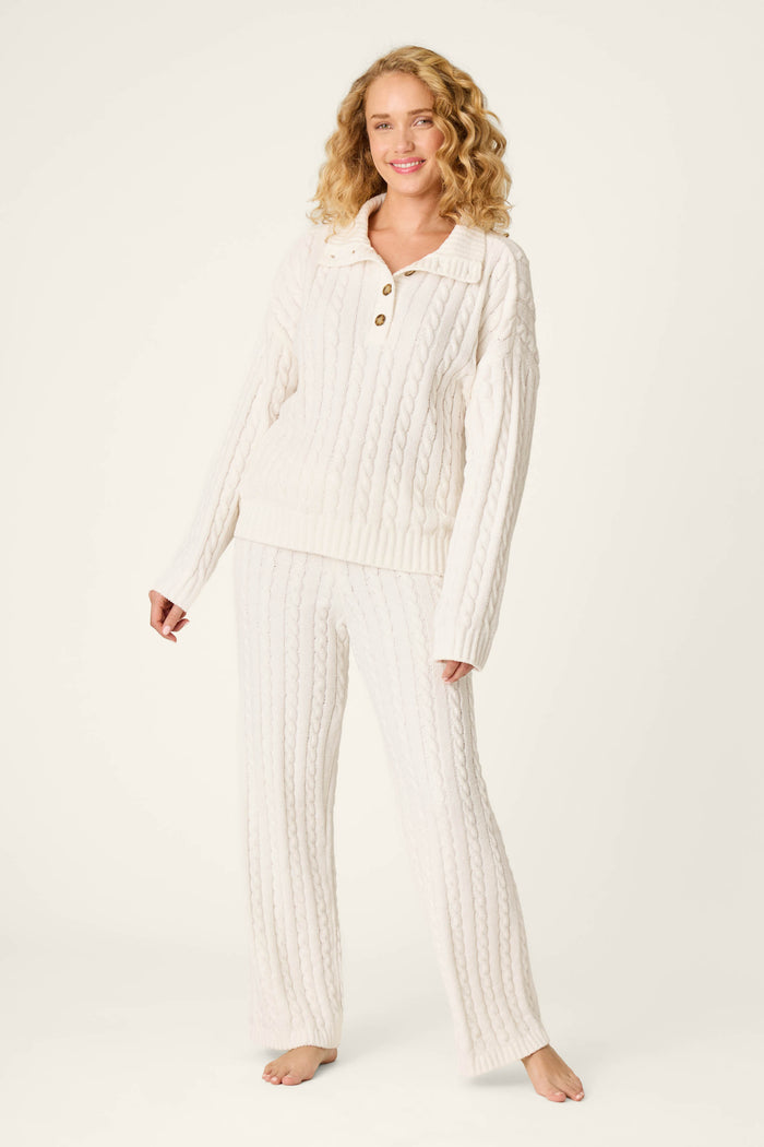 A woman stands barefoot on a plain background, smiling with her hands relaxed by her sides, wearing the P.J. Salvage Cozy Chenille Cable Knit Ivory Pullover.