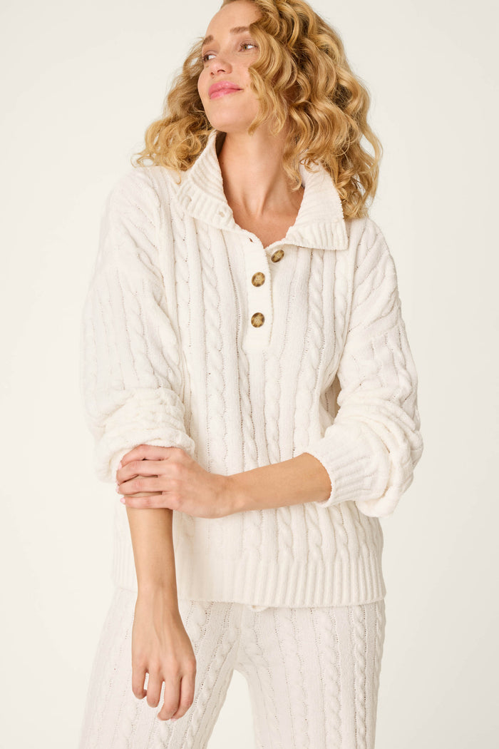 A woman wears the P.J. Salvage Cozy Chenille Cable Knit Ivory Pullover, featuring a collar and wooden buttons, paired with matching knit pants against a plain light background.