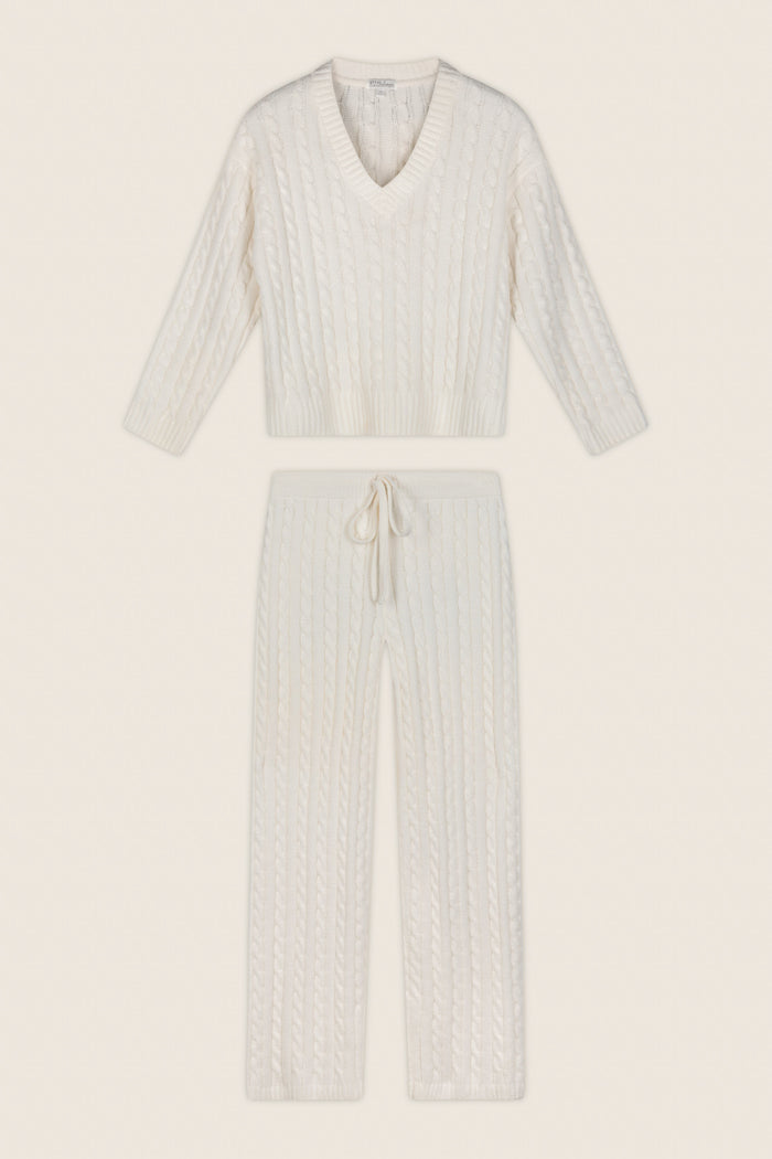 A two-piece knit loungewear set in an off-white/cream color, featuring a long-sleeve V-neck sweater and matching drawstring pants, laid flat against a solid cream background.