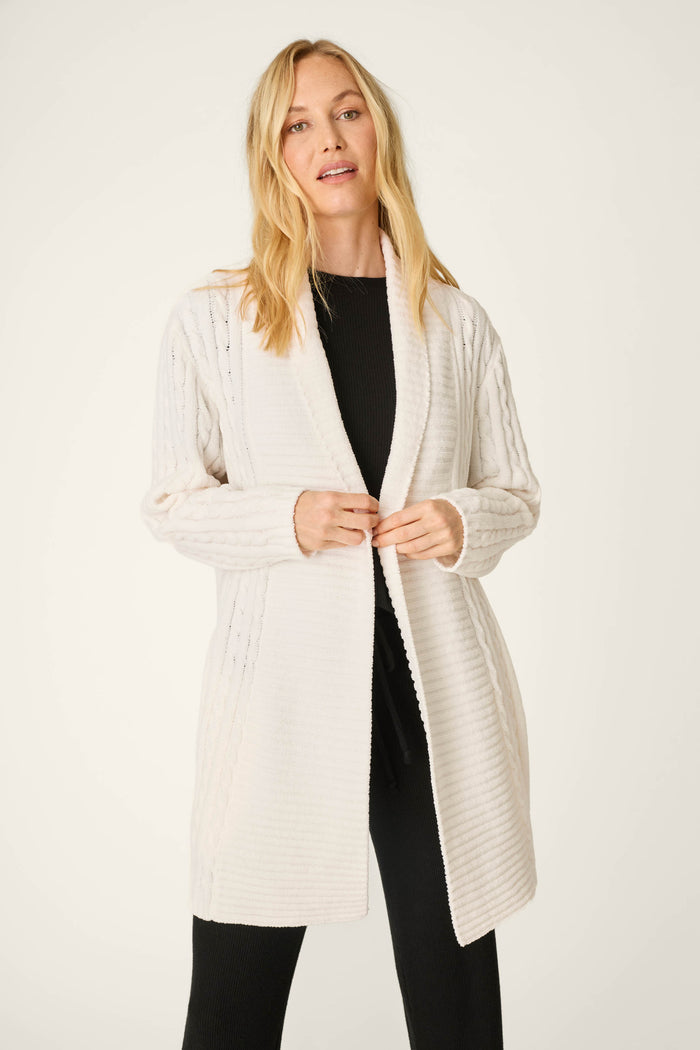 A woman wearing the P.J. Salvage Cozy Chenille Cable Knit Long Ivory Cardigan over a black outfit stands against a plain light background, facing the camera with a relaxed expression.