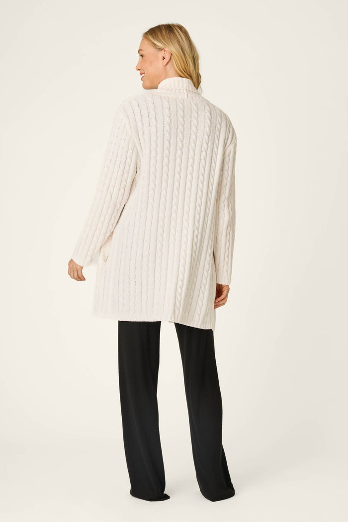 A person stands facing away, wearing the P.J. Salvage Cozy Chenille Cable Knit Long Ivory Cardigan paired with black pants, set against a plain light-colored background.