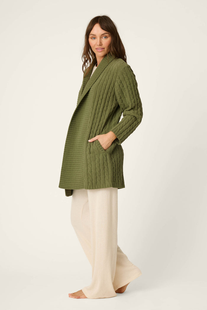 A woman wearing the P.J. Salvage Cozy Chenille Cable Knit Long Olivine Cardigan paired with cream wide-leg pants stands barefoot against a plain light background.