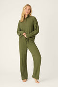 A woman stands barefoot against a plain background, looking at the camera with a relaxed pose, wearing the Cozy Chenille Cable Knit Olivine Pullover Lounge Set by P.J. Salvage.