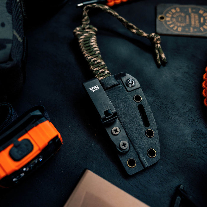 Discreet Carry Pocket Clip attached to a tactical knife, featuring a black finish and paracord handle, on a dark surface.