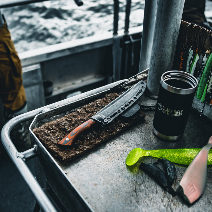 Flathead Fillet knife with Kydex sheath on a boat table, alongside fishing gear and a coffee tumbler.