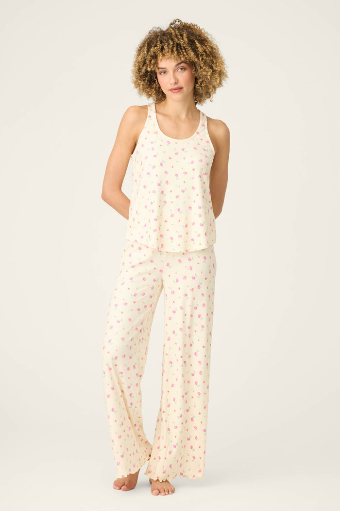 A person stands barefoot against a plain background, wearing the P.J. Salvage For the Mamas Butter Blooms Long PJ Set—a butter yellow sleeveless top and wide-leg pants with a small pink floral pattern.
