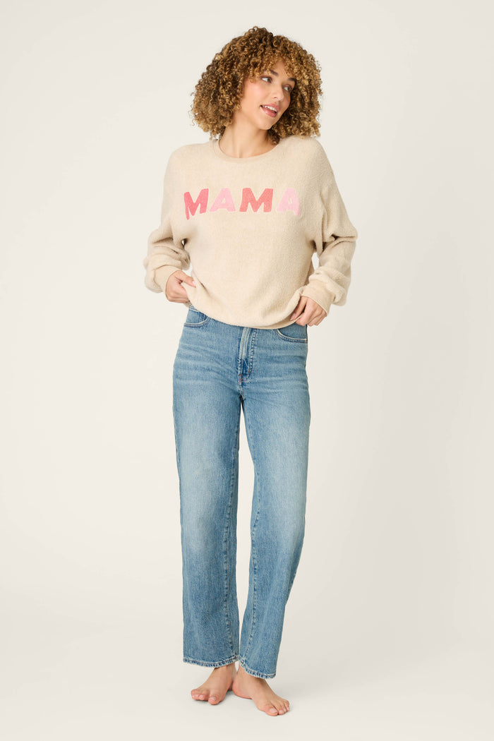 A person with curly hair stands barefoot against a plain background, wearing the P.J. Salvage For the Mamas Sweetheart Mama Sweatshirt in light oatmeal and blue jeans, hands in their pockets and looking to the side.