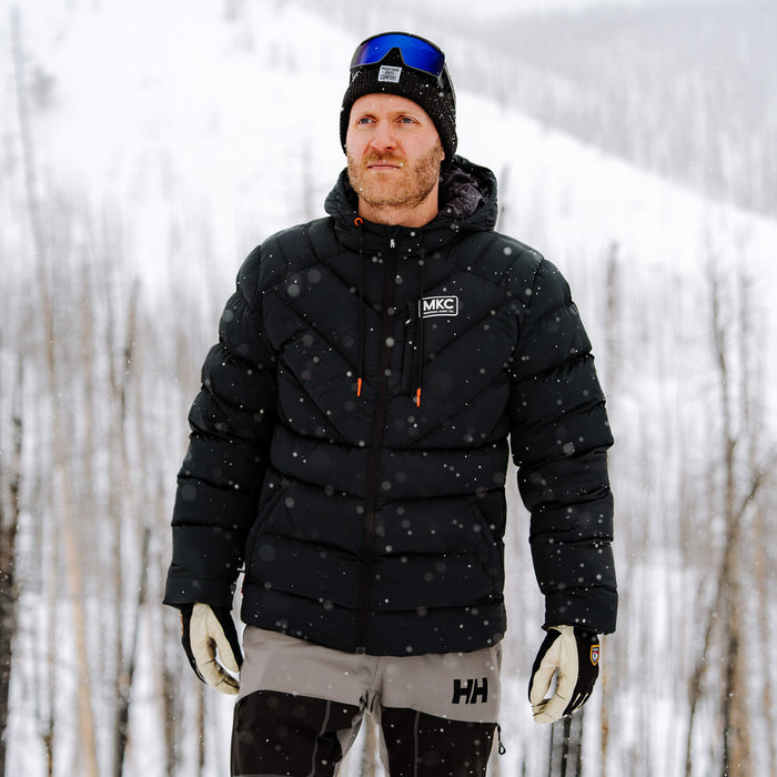 Man wearing a black Grinnell Puffy Zip Jacket in a snowy outdoor setting, showcasing warmth and durability for outdoor activities.