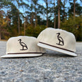 Cream colored hat with brown embroidered heron on the crown and rope stretched across the bill.