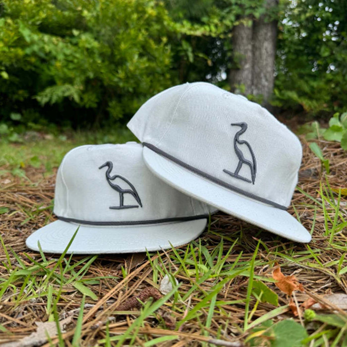 White hat with grey embroidered heron on the crown and grey rope stretched across the bill.