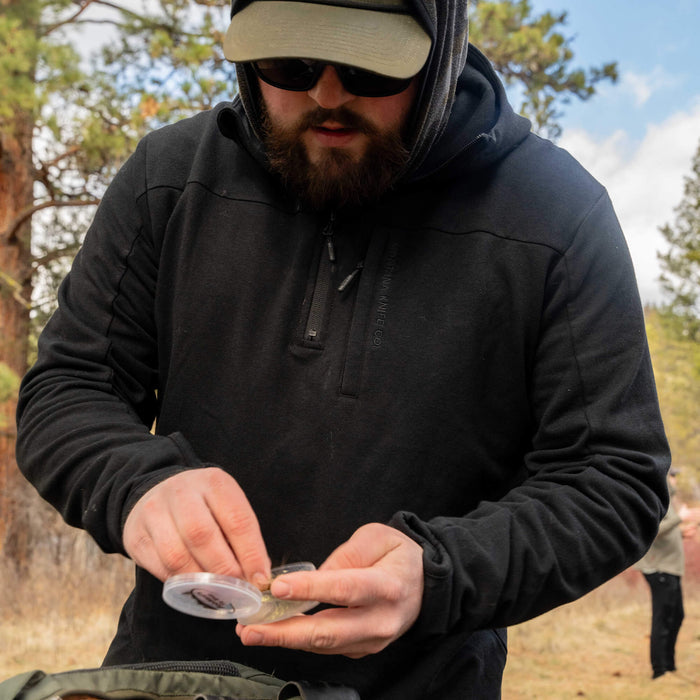 Man wearing a black Highline half-zip hoodie, focused on preparing gear outdoors in a natural setting.