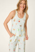 A woman smiles with one hand in her pocket, wearing the P.J. Salvage It's Five O'clock Somewhere Cocktail Print Tank Top—a sleeveless, light-colored pajama top featuring colorful tropical drinks and fruits.