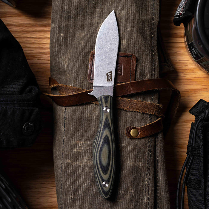 JACKSTONE knife with a green and black handle, resting on a canvas roll, showcasing its sleek blade and craftsmanship.