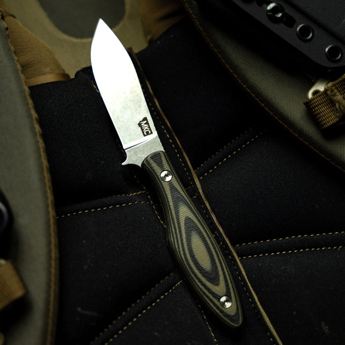 Green and black JACKSTONE knife resting on a tactical seat, featuring a sleek blade and ergonomic handle.