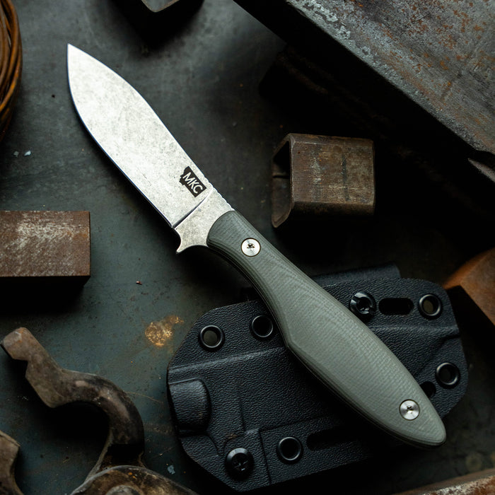 JACKSTONE knife in grey with a textured handle, displayed on a rugged surface with metal tools and accessories.