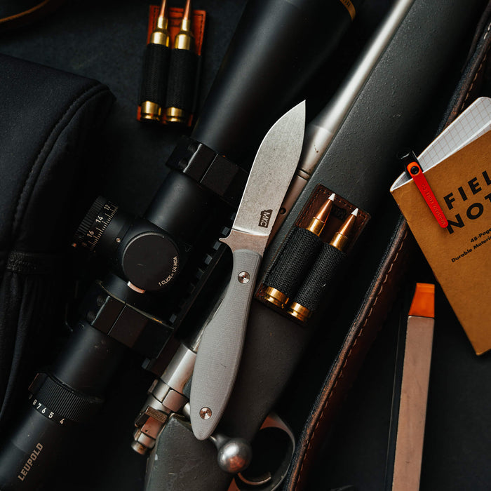 JACKSTONE knife in grey resting on a rifle with ammunition, showcasing its sleek design and functionality for outdoor enthusiasts.