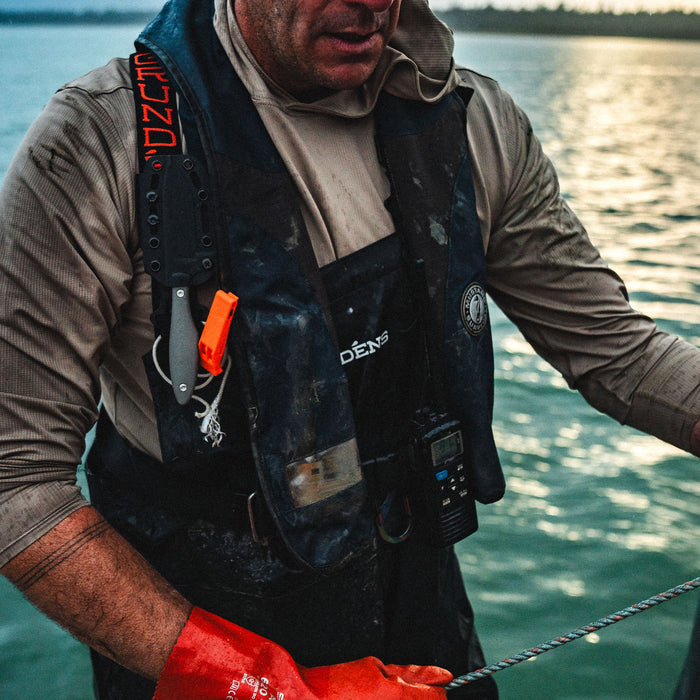A person wearing a grey JACKSTONE knife sheath and red gloves, working on a boat near water.
