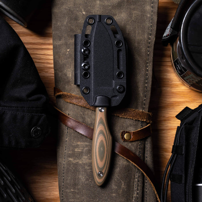 JACKSTONE knife in olive and tan with a black sheath, displayed on a canvas background with outdoor gear.