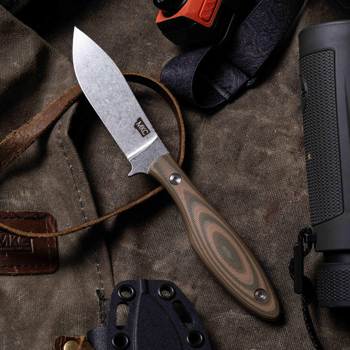 Olive and tan JACKSTONE knife with a rugged blade, set on a textured background of outdoor gear and tools.
