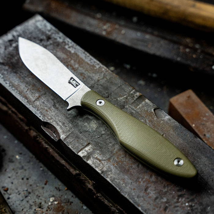 Olive green handled JACKSTONE knife resting on a metal work surface, showcasing its sharp blade and durable design.