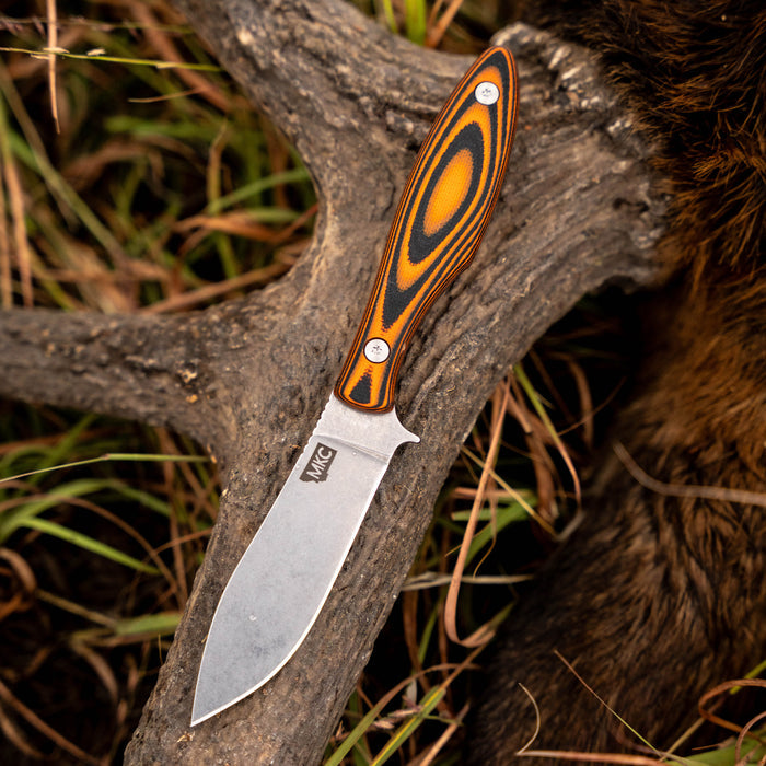 JACKSTONE knife with an orange and black handle, resting on a rustic antler, showcasing its durable blade design.