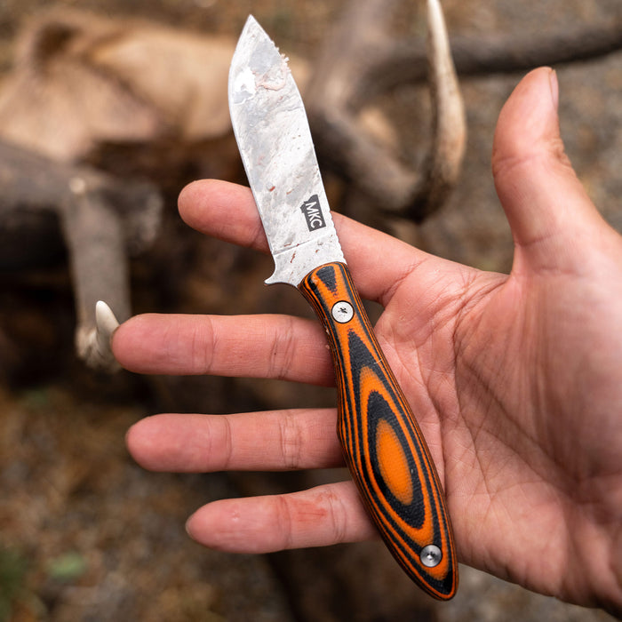 JACKSTONE knife with an orange and black handle, featuring a stainless steel blade, held in a hand outdoors.