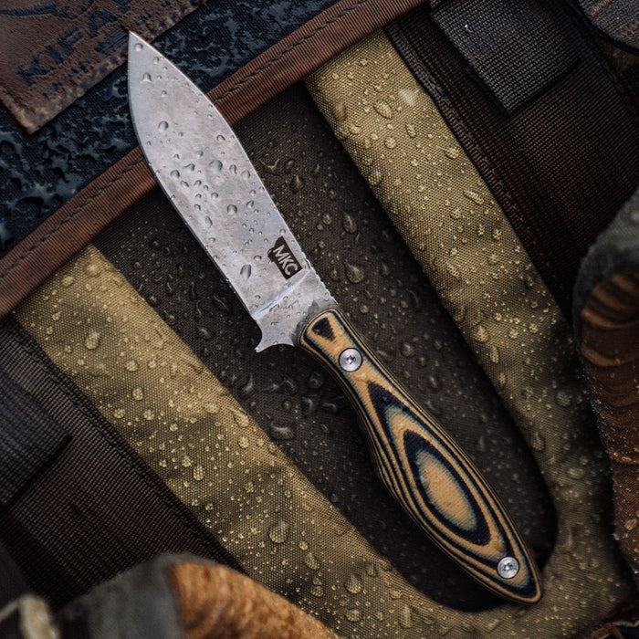JACKSTONE knife in tan and black with a textured blade, resting on a water-resistant surface. Ideal for outdoor use.